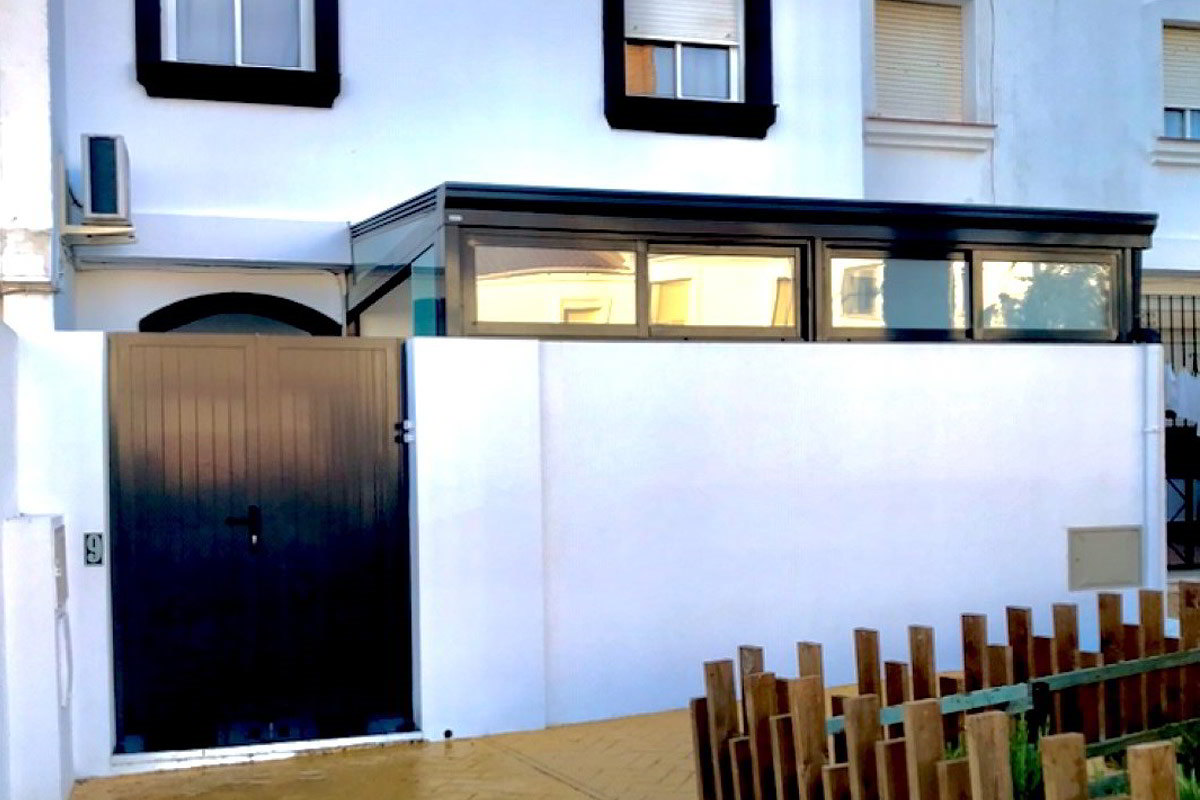 White facade of a semi-detached house with a black door, large windows and stone floor, Las Gaviotas urbanization.