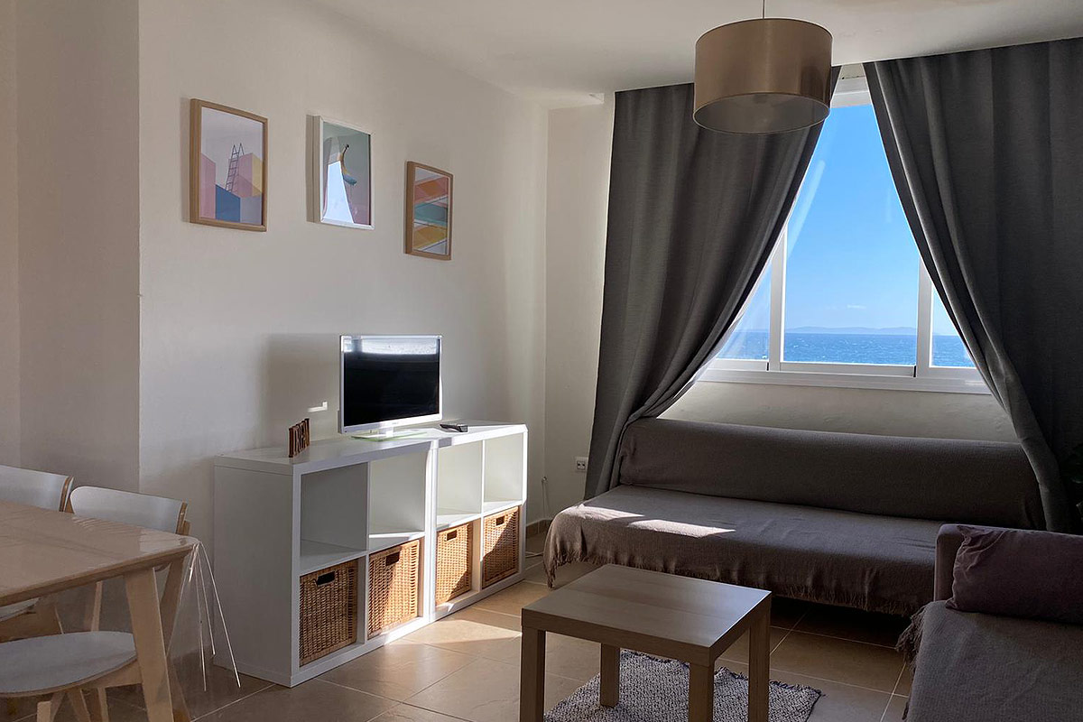 Salón con sofá cama y ventanales con vistas al mar.